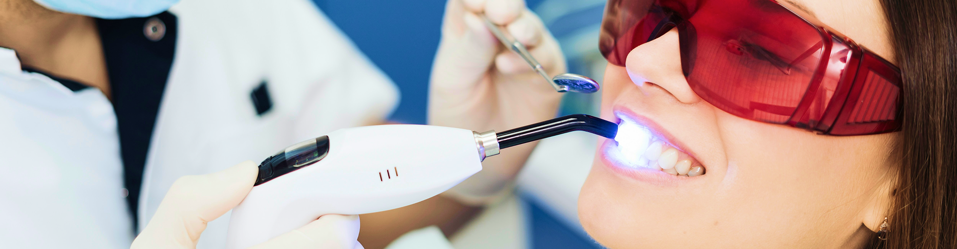 Gloved hands shining light onto teeth of woman wearing orange glasses.